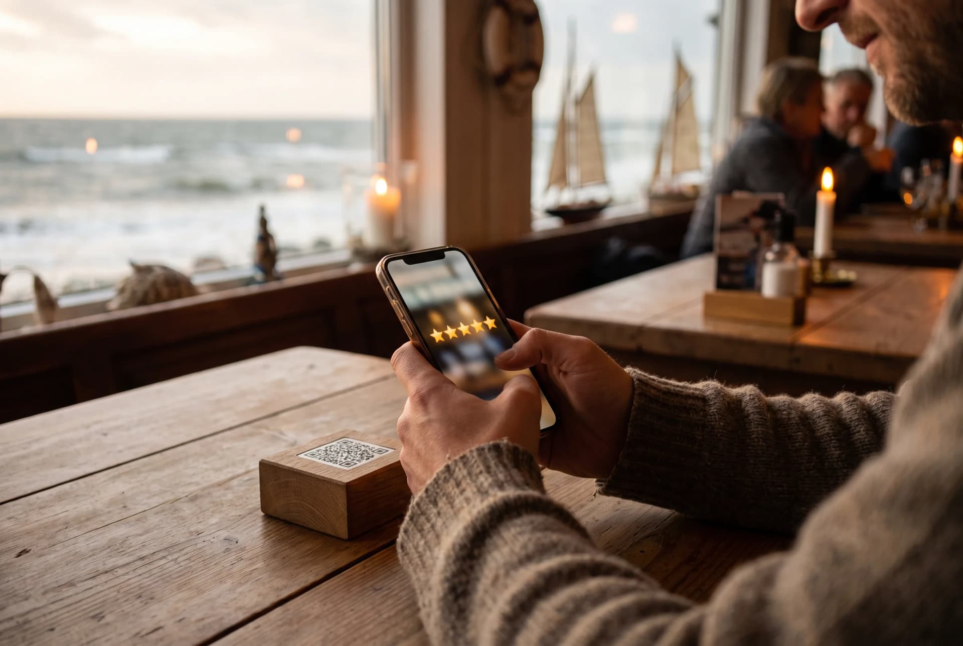 Gast scannt an einem Restauranttisch an der Küste einen QR-Code-Tischaufsteller und bewertet mit fünf Sternen