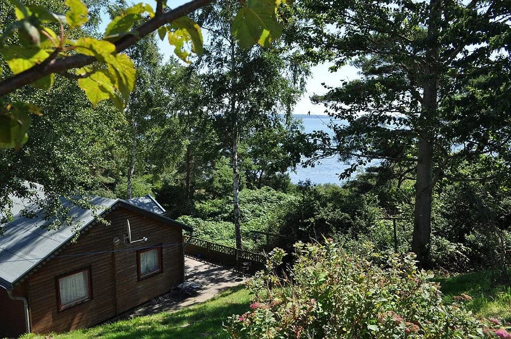 Holzhütte mit Blick auf den Bodden zwischen Bäumen, Inselcamp Rügen
